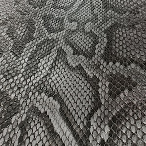 Op de afbeelding: Close-up van een getextureerd oppervlak met een slangenpatroon. Het patroon heeft een mix van grijze en zwarte schubben, waardoor een realistisch en gedetailleerd ontwerp ontstaat. De schubben variëren in grootte en vorm.