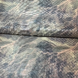 Pode incluir: Close-up de um pedaço de pele de réptil com um padrão de escamas. A pele tem uma aparência manchada com tons de cinza, azul e marrom. A textura é áspera e detalhada, com escamas visíveis. A aparência geral é natural e texturizada.