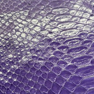 May include: Close-up of a textured, purple material with a scale-like pattern. The surface has a glossy sheen, with highlights creating a three-dimensional effect. The design resembles reptile skin.