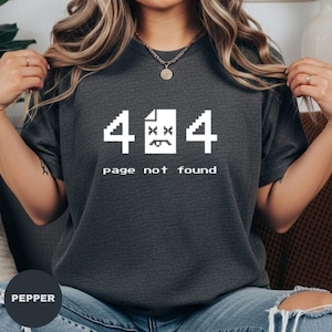 May include: Dark gray t-shirt with a white graphic of the number 4, a sad-faced document, and the number 4. Below the graphic, the text reads "page not found". The shirt is a crew neck.