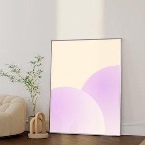 Könnte beinhalten: Ein gerahmter Kunstdruck mit abstrakter Kunst, der einen Farbverlauf aus weichen Lavendel- und Cremefarben zeigt. Das Kunstwerk hat ein minimalistisches Design mit abgerundeten Formen. Der Druck wird in einem modernen Innenraum mit Holzboden und einer kleinen Pflanze ausgestellt.