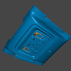 May include: A blue plastic car interior component, possibly a roof console, with a rectangular recessed area containing several buttons and lights. The component has a textured surface and appears to be a 3D scan or model.