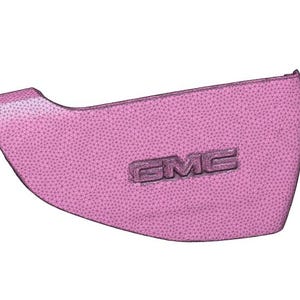 May include: A pink, curved automotive part with the embossed letters "GMC". The part has a textured surface and a unique shape, possibly a door panel or interior trim piece.