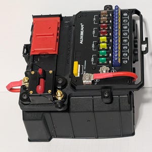 May include: A black Auxbeam electrical switch panel system featuring a red 80A circuit breaker, a red battery terminal cover, and a vertical row of multi-colored automotive fuses labeled 5A, 10A, 20A, and 30A alongside a blue terminal block.