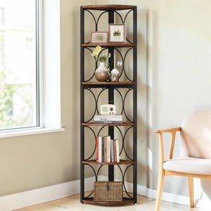 May include: A tall, corner bookshelf with five shelves. The shelves are made of dark wood and supported by a black metal frame with decorative arched accents. The shelves are filled with books, decorative items, and framed pictures. The bookshelf is placed next to a window.