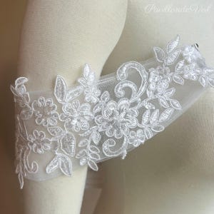 May include: White floral lace sleeve detail. The delicate lace features embroidered flowers and leaves. The sheer fabric is attached to a mannequin arm. The text "Pavillon de Veil" is visible in the upper right corner.