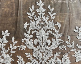 May include: A sheer white bridal veil featuring intricate white floral embroidery with a symmetrical damask-inspired pattern. The delicate tulle fabric is adorned with detailed leaf and vine motifs. The text Pavillonde Veil is visible.
