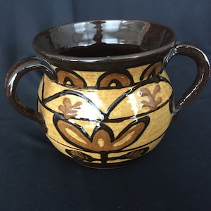 May include: A brown ceramic pot with two handles and a decorative design of brown and tan stylized flowers and leaves.