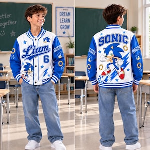 Könnte beinhalten: Eine weiß-blaue Collegejacke mit Sonic the Hedgehog-Grafiken, dem Namen Liam, der Zahl 6 und goldenen Ring-Symbolen. Die Rückseite zeigt eine große Sonic-Figur mit dem Schriftzug SONIC, während die Vorderseite Druckknöpfe und gestreifte Bündchen hat.