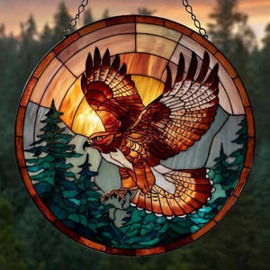 May include: Circular stained glass window depicting a hawk in flight. The hawk's feathers are brown, orange, and white, set against a sunset, mountains, and evergreen trees. The window has a dark border and a chain for hanging, with a diameter of approximately 30 cm.