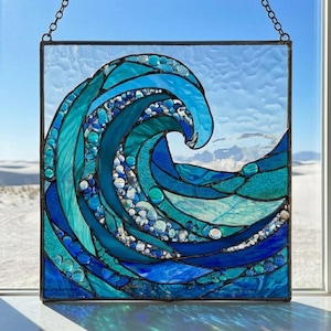 May include: Stained glass panel depicting a stylized ocean wave in shades of blue and teal. The wave crests with a foamy edge, and the design incorporates various textures and shapes of glass. A metal chain is attached for hanging.