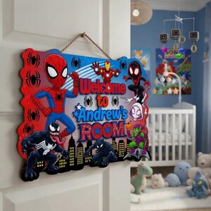 May include: A rectangular wooden wall sign featuring a colourful Marvel superhero theme with Spider-Man, Iron Man, Venom, Black Panther, and Green Goblin. The text reads Welcome to Andrew's ROOM in bold blue and red lettering with spider icons.