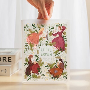 Könnte beinhalten: Ein klarer, rechteckiger Aufbewahrungsbehälter mit Illustrationen aus "Little Women". Das Design zeigt vier Figuren in Kleidern, grünes Laub und den Titel "Little Women". Der Behälter wird von einer Hand gehalten.