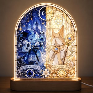 Pode incluir: Um painel de luz LED arqueado com um design de vitral dividido em seções azul e dourada. O lado esquerdo retrata Shadow Milk Cookie com um ícone de espadas, e o lado direito mostra Pure Vanilla Cookie com um ícone de paus e motivos florais.