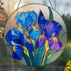May include: A circular stained glass panel depicting blue and purple iris flowers with yellow highlights and green foliage. The artwork is framed with a black metal border and suspended by a chain. The background is a textured, translucent glass.