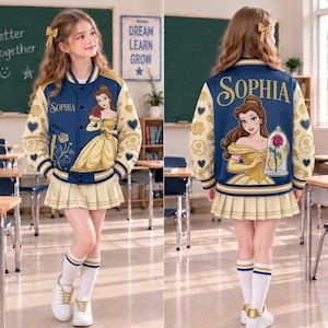 Puede incluir: Una chaqueta universitaria azul marino y crema con el nombre Sophia, un gráfico de Bella de La Bella y la Bestia, y patrones de rosas y corazones dorados en las mangas. La chaqueta se combina con una falda plisada crema y calcetines.