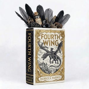 Puede incluir: Un libro decorativo titulado "Fourth Wing" de Rebecca Yarros, con una ilustración de dragón. El libro está adornado con plumas negras y grises, pequeñas piedras y un vial etiquetado como "Dagger Tears".