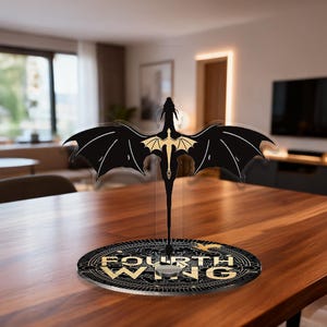 Puede incluir: Una pantalla acrílica con forma de dragón negro y dorado. El dragón tiene alas extendidas y una cola larga, con el texto "FOURTH WING" en la base. El cuerpo del dragón es dorado y las alas son negras.