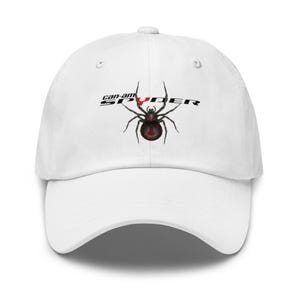 Könnte beinhalten: Weiße Baseballkappe mit dem Text "Can-Am Spyder" und einer schwarz-roten Spinnengrafik. Die Kappe hat einen gebogenen Schirm und ein klassisches Sechs-Panel-Design, geeignet für Outdoor-Aktivitäten.