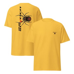 Pode incluir: Camisetas amarelo mostarda. Uma camisa apresenta um gr&aacute;fico de aranha preta e vermelha com o texto "Spyder" e "can-am" na vertical. A outra camisa tem um gr&aacute;fico de aranha menor no peito.