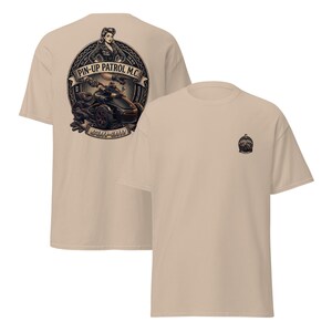 Puede incluir: Dos camisetas color beige. Una tiene un gran dise&ntilde;o circular en la espalda con una pin-up, una motocicleta y el texto "PIN-UP PATROL M.C." y "CAN-AM". La otra tiene un dise&ntilde;o m&aacute;s peque&ntilde;o en la parte delantera.