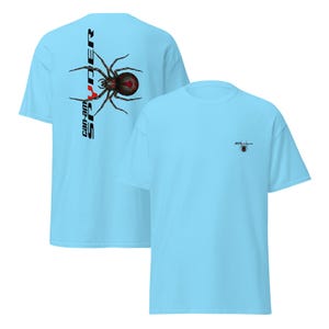 Pode incluir: T-shirts azuis claros com um gr&aacute;fico de aranha. Uma camisa apresenta um grande design de aranha com o texto "can-am SPYDER" verticalmente no lado esquerdo. A outra camisa tem um pequeno gr&aacute;fico de aranha no peito.