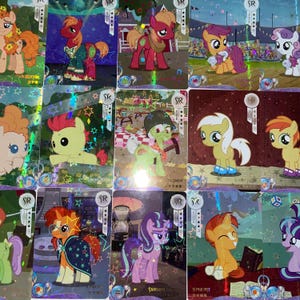 May include: A selection of vibrant trading cards showcasing cartoon ponies. Each card displays a unique design with various coloured ponies, stars, and decorative features. Some cards include text, such as "SR" and "SUNBURST".
