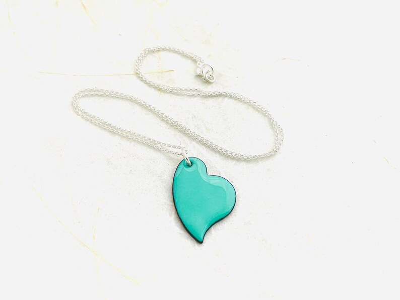 May include: A silver chain necklace with a teal blue heart pendant.