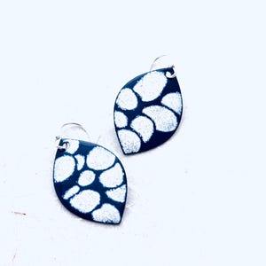 May include: A pair of leaf-shaped earrings with a dark blue background and a white, speckled pattern. The earrings have silver-colored hooks. The design is a modern take on a classic shape, suitable for everyday wear or special occasions.