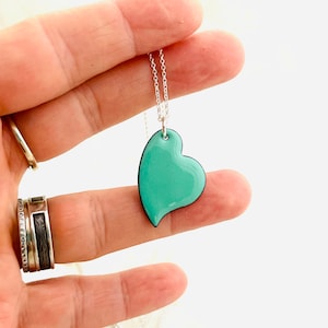 May include: A silver chain necklace with a turquoise blue heart pendant. The heart is slightly asymmetrical and has a black outline.