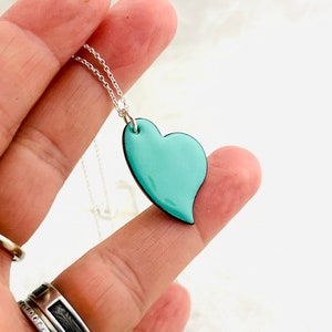 May include: A silver chain necklace with a light blue heart pendant. The heart is slightly asymmetrical and has a smooth, glossy finish.