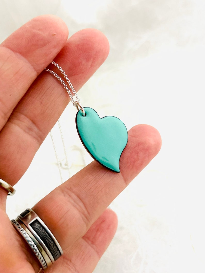 May include: A silver chain necklace with a light blue heart pendant. The heart is slightly asymmetrical and has a smooth, glossy finish.