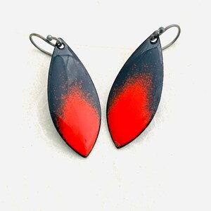 May include: A pair of black and red enamel earrings with a teardrop shape. The earrings have a black background with a red gradient that fades to a darker red at the bottom.