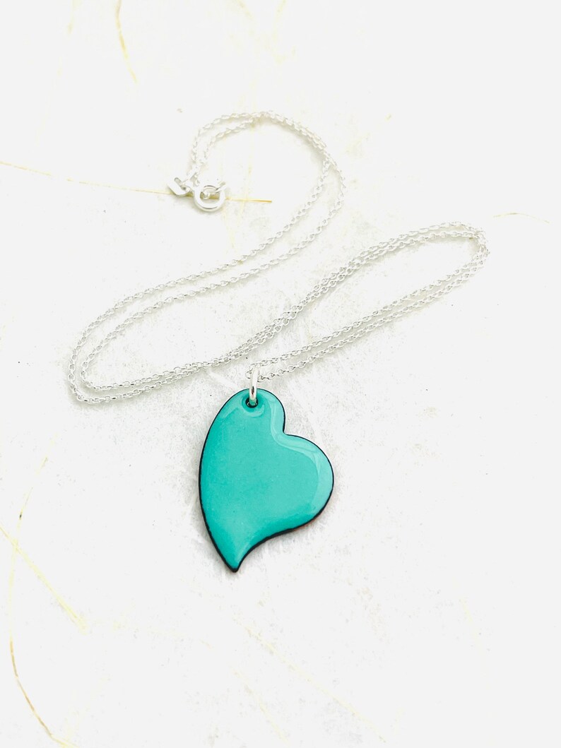 May include: A silver chain necklace with a turquoise heart pendant. The heart is a simple, modern design with a smooth, glossy finish.