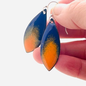 May include: A pair of dangle earrings with a teardrop shape. The earrings are made of metal and have a blue and orange enamel finish.