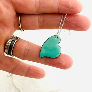 May include: A silver chain necklace with a teal blue heart pendant. The heart is slightly asymmetrical and has a black outline.