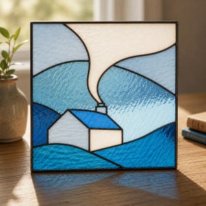 May include: A square stained glass panel featuring a landscape scene with a small white house with a blue roof. A thin trail of smoke rises from the chimney into a pale sky. The design uses various shades of blue and white glass with dark lead lines.