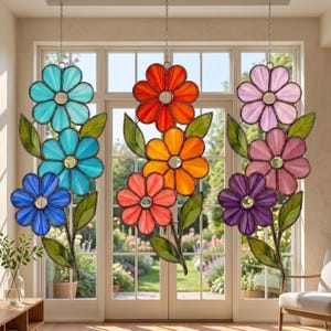 Op de afbeelding: Gebrandschilderde bloemvormige raamhangers in blauwe, oranje en paarse tinten. Elke bloem heeft een spiegelend midden en groene bladeren. De bloemen hangen aan kettingen, wat een decoratieve weergave creëert.