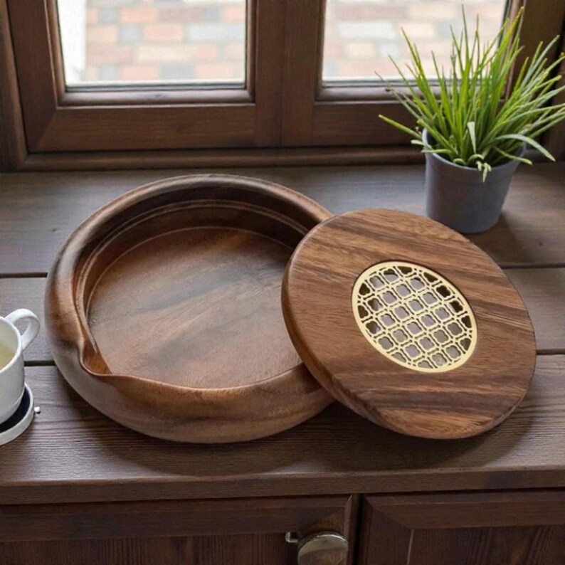 May include: A wooden serving bowl with a matching lid. The lid features a decorative gold-colored metal insert. The bowl and lid are made of a dark brown wood. The bowl is open, and the lid is partially covering it.