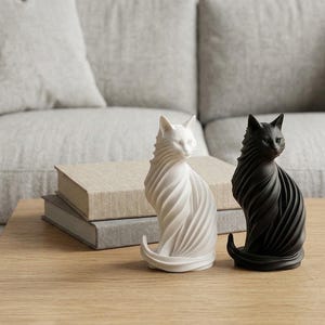 May include: Two cat figurines, one in matte white and one in matte black, featuring a stylized, swirling, ribbed texture across their bodies. The cats are depicted in a seated position with their tails curled around their bases, showcasing a smooth finish.