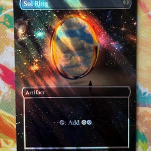 May include: A rectangular trading card titled Sol Ring featuring a holographic space background with stars and nebulae. A golden ring floats above a dark horizon with a small silhouette figure. The card text includes Artifact and the symbol for adding colorless mana.