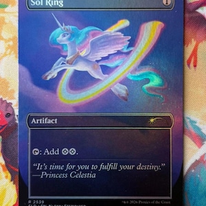 以下が含まれることがあります： Sol Ringというタイトルの長方形のMagic: The Gatheringトレーディングカード。虹色のたてがみと尻尾を持つ翼のあるユニコーンがカラフルな弧を描いて飛んでいる様子が描かれています。カードにはArtifactというテキスト、能力シンボル、Princess CelestiaによるIt's time for you to fulfill your destinyという引用が含まれています。