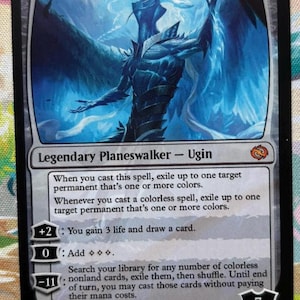 May include: A Magic: The Gathering card featuring Ugin, Eye of the Storms. The card has a black border with a blue and white illustration of a spectral figure. Text includes the card's name, type, and abilities.