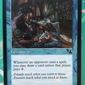 May include: A blue Magic: The Gathering card named "Rhystic Study." The card shows an illustration of a person reading, with text that reads "Whenever an opponent casts a spell, you may draw a card unless that player pays 1."