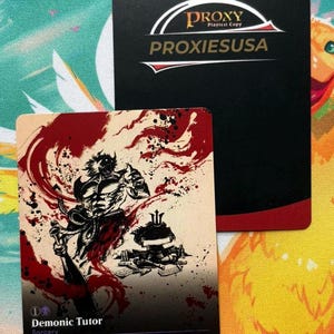 May include: A rectangular game card featuring a black and red ink-style illustration of a figure and armor, titled Demonic Tutor, with a secondary black card behind it displaying the text Proxy Playtest Copy PROXIESUSA in white and gold.
