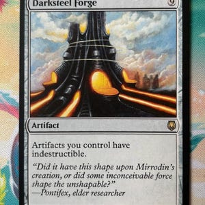 Może przedstawiać: Karta kolekcjonerska Darksteel Forge przedstawiająca czarną, metaliczną strukturę przypominającą wieżę, z której podstawy wydobywa się jasne pomarańczowe światło na tle zachmurzonego nieba. Tekst na karcie brzmi: Artifacts you control have indestructible.