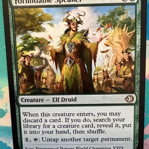 Może przedstawiać: Karta Magic: The Gathering zatytułowana "Formidable Speaker". Karta przedstawia ilustrację postaci podobnej do elfa w zielonych i brązowych szatach, z innymi postaciami w tle. Tekst karty zawiera instrukcje gry i nazwisko Jean-Emmanuel Depraz.