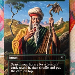 Op de afbeelding: Een rechthoekige ruilkaart getiteld Worldly Tutor met een illustratie van een ouder persoon met een witte baard en tulband die een rode edelsteen en een staf met een draak vasthoudt. De kaarttekst luidt Instant en Search your library for a creature card, reveal it, then shuffle and put the card on top.