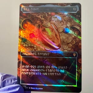 Puede incluir: Una tarjeta coleccionable rectangular con acabado holográfico que muestra un gran colgante de color ámbar sobre un montón de monedas de oro y piedras preciosas. La tarjeta presenta texto rúnico en la parte superior e inferior con un cero.