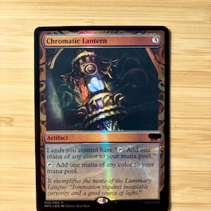 May include: A foil Magic: The Gathering trading card titled Chromatic Lantern. The card features an ornate, glowing lantern illustration, the text 'Artifact', and game rules regarding mana production. It has a metallic, reflective finish.